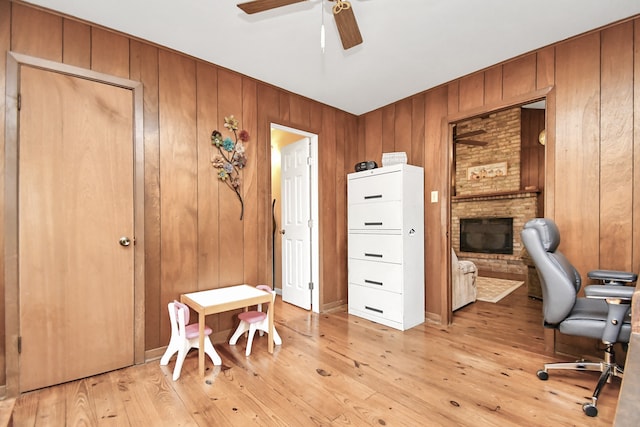 home office with a fireplace, light wood-type flooring, ceiling fan, and wood walls