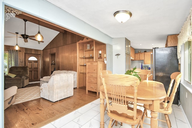 dining area with ceiling fan, wood walls, light hardwood / wood-style floors, and vaulted ceiling