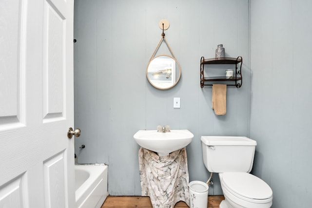 bathroom with a tub, wooden walls, sink, and toilet