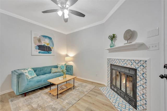 living room featuring hardwood / wood-style floors, ceiling fan, ornamental molding, and a tiled fireplace