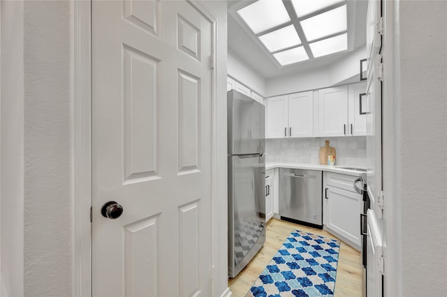 kitchen featuring backsplash, white cabinets, light wood-type flooring, and appliances with stainless steel finishes