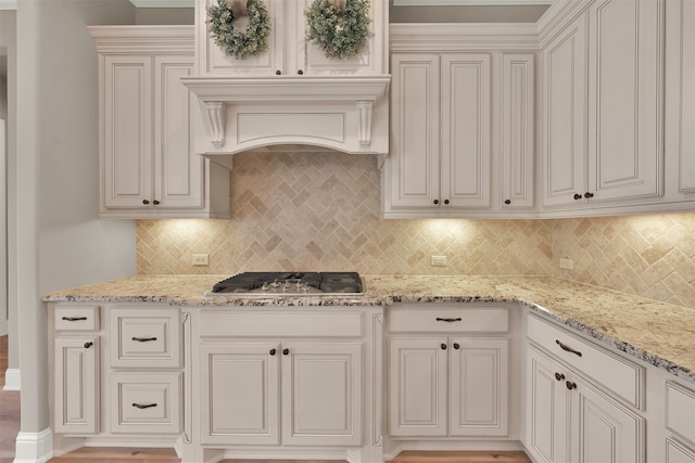 kitchen featuring light stone counters, premium range hood, backsplash, and stainless steel gas stovetop