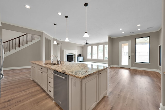 kitchen featuring ceiling fan, pendant lighting, stainless steel dishwasher, a center island with sink, and sink