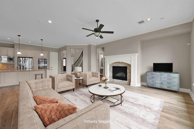 living room with light wood-type flooring, ceiling fan, crown molding, and a fireplace