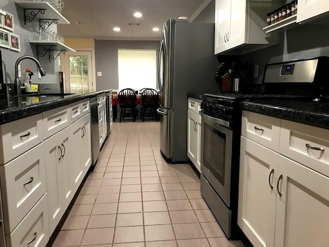 kitchen featuring stainless steel appliances, light tile patterned floors, crown molding, dark stone counters, and white cabinets