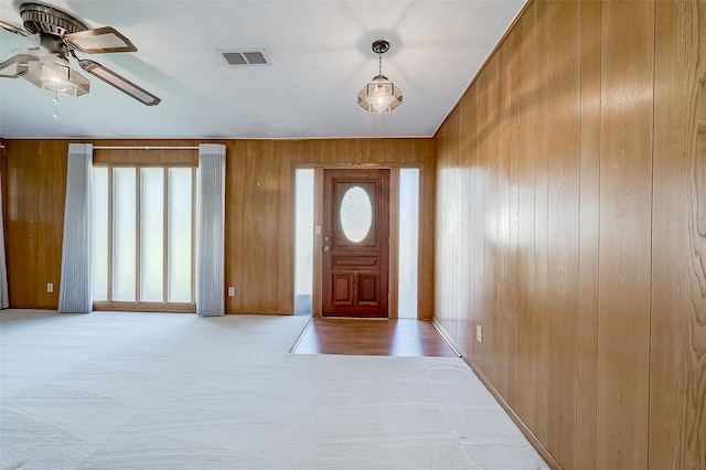 carpeted entryway with ceiling fan and wood walls