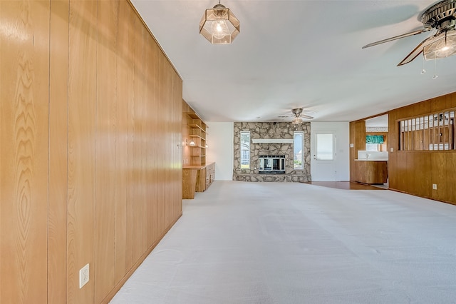 carpeted living room with a stone fireplace, ceiling fan, and wood walls