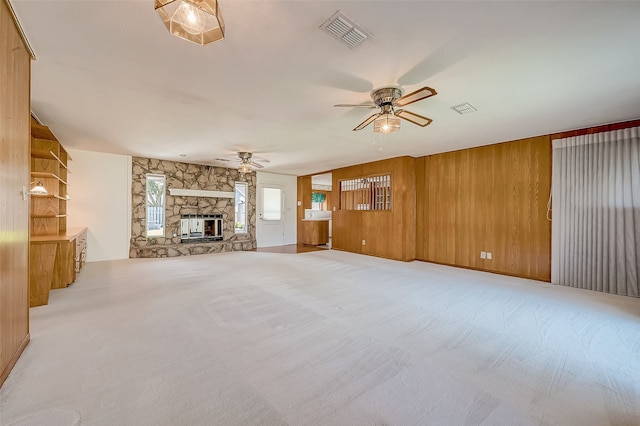 unfurnished living room featuring a fireplace, light carpet, ceiling fan, and wood walls