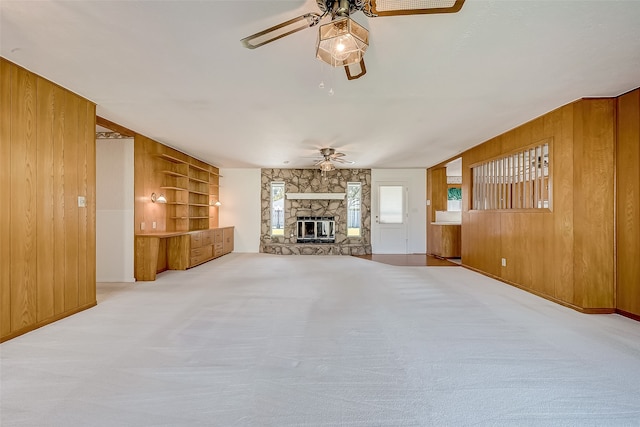 unfurnished living room featuring light carpet, a fireplace, and wood walls