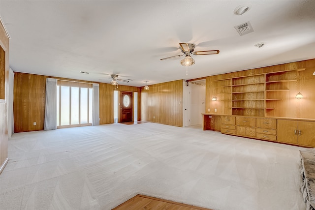 unfurnished living room featuring light colored carpet, ceiling fan, and wooden walls