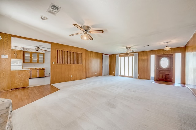 unfurnished living room with wood walls, light carpet, and vaulted ceiling