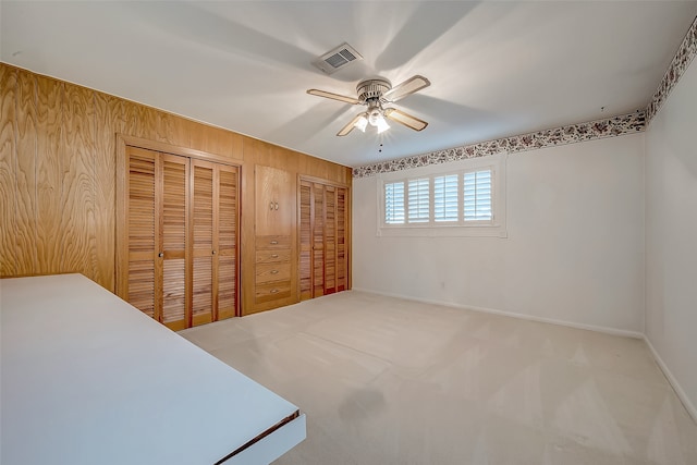 carpeted bedroom with wooden walls, ceiling fan, and two closets