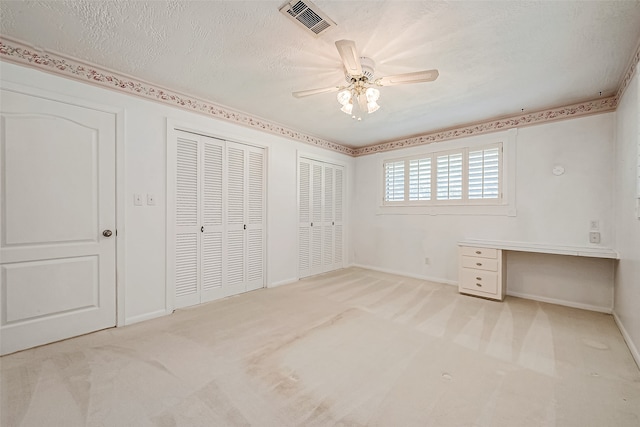 unfurnished bedroom with light carpet, a textured ceiling, ceiling fan, and multiple closets