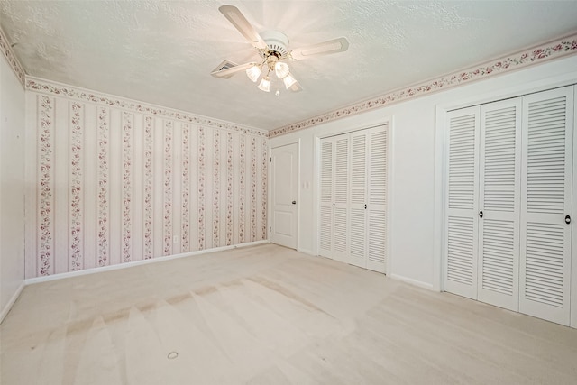 unfurnished bedroom featuring two closets, ceiling fan, light colored carpet, and a textured ceiling