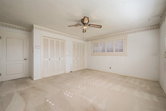 unfurnished bedroom featuring a textured ceiling, two closets, ceiling fan, and light colored carpet