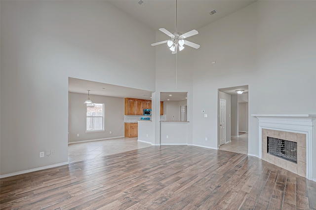 unfurnished living room with a fireplace, light wood-type flooring, high vaulted ceiling, and ceiling fan