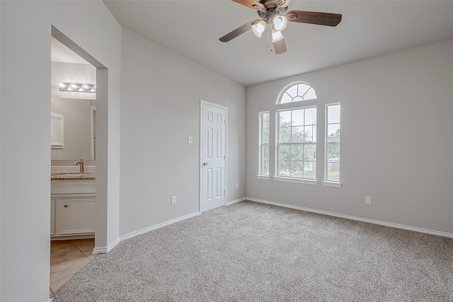 unfurnished bedroom featuring a closet, light colored carpet, ensuite bath, and ceiling fan