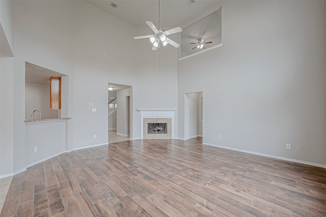 unfurnished living room with a fireplace, light hardwood / wood-style floors, high vaulted ceiling, and ceiling fan