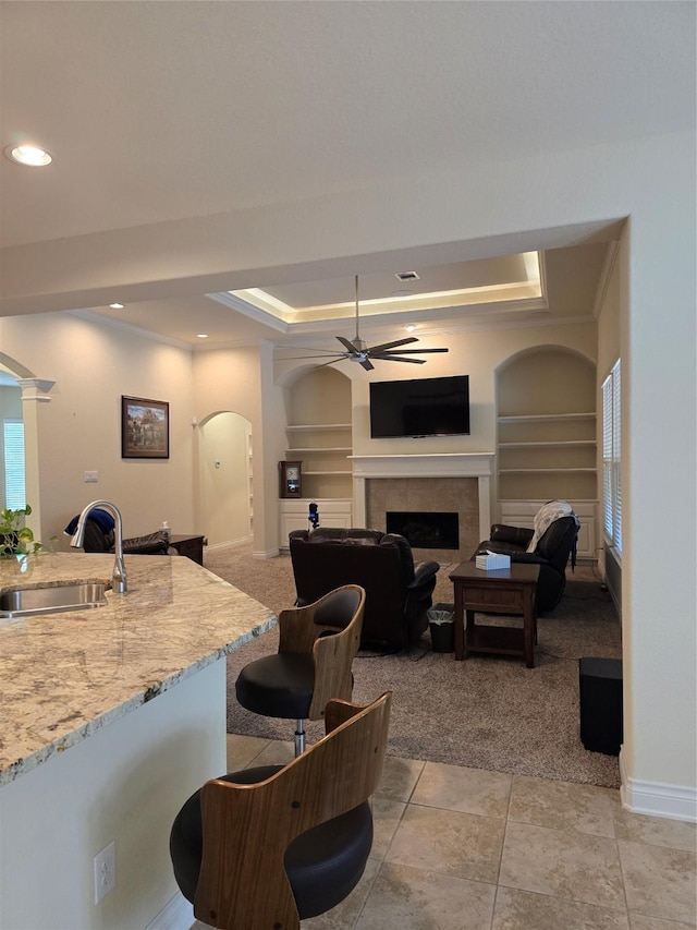 kitchen with sink, a tile fireplace, built in features, and a raised ceiling