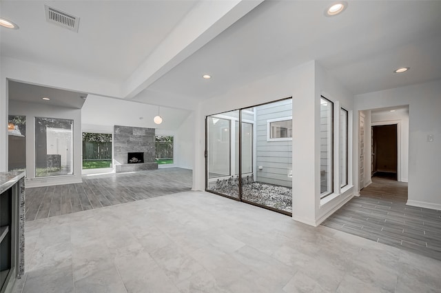 unfurnished living room featuring beam ceiling, a tiled fireplace, and light wood-type flooring