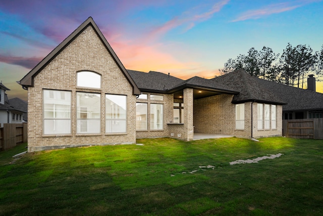 back house at dusk with a patio area and a yard