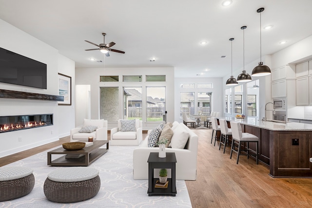 living room featuring light wood-type flooring, ceiling fan, and sink