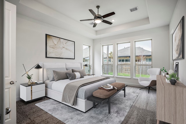 bedroom with dark colored carpet, ceiling fan, and a raised ceiling