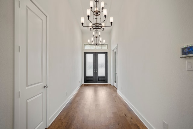 foyer entrance with french doors, hardwood / wood-style flooring, and an inviting chandelier