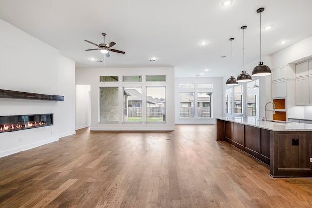 kitchen with ceiling fan, sink, light stone counters, hardwood / wood-style floors, and decorative light fixtures