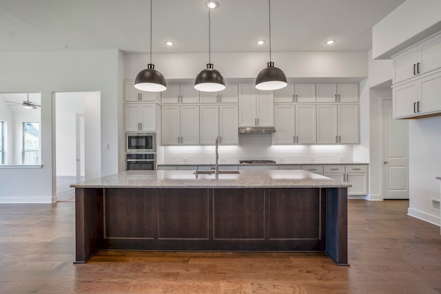 kitchen with pendant lighting, a kitchen island with sink, dark wood-type flooring, sink, and light stone countertops