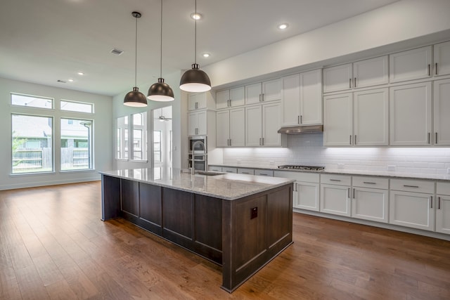 kitchen featuring light stone countertops, decorative light fixtures, a center island with sink, and dark hardwood / wood-style floors