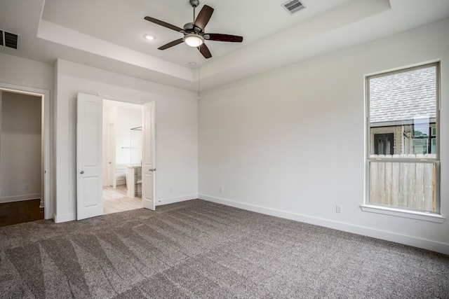 unfurnished bedroom with carpet flooring, ceiling fan, a raised ceiling, and ensuite bath