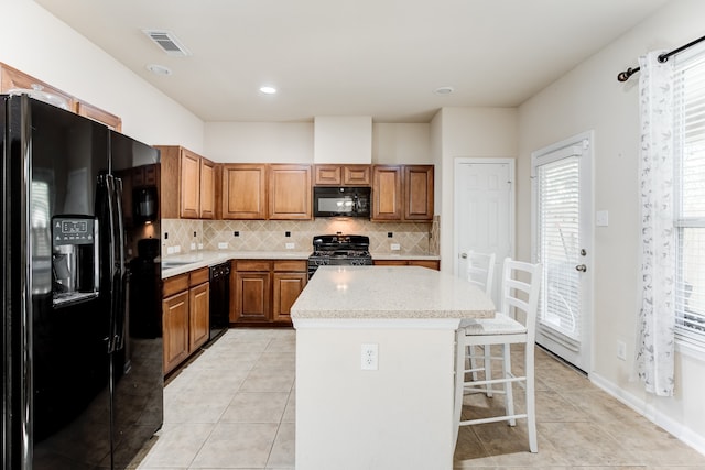 kitchen featuring a kitchen island, tasteful backsplash, a breakfast bar area, light tile patterned flooring, and black appliances