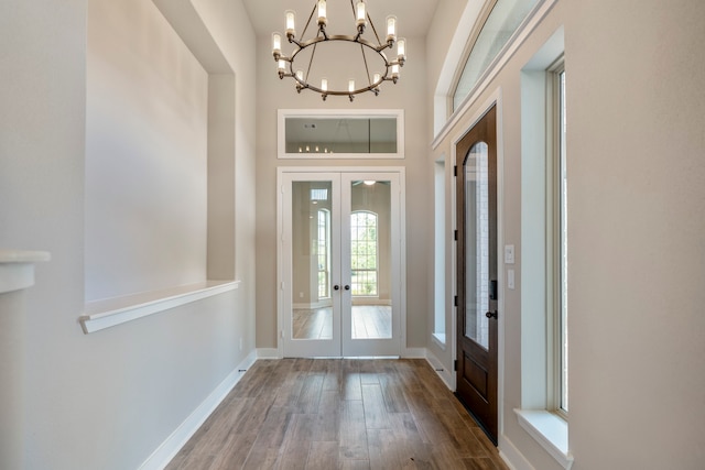 foyer entrance featuring french doors, wood-type flooring, and an inviting chandelier