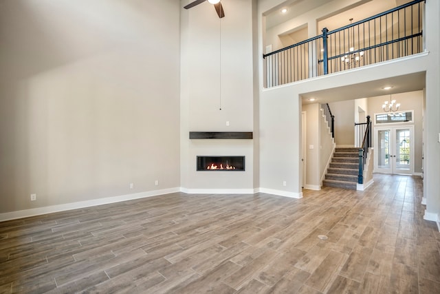 unfurnished living room with ceiling fan, french doors, a towering ceiling, and wood-type flooring