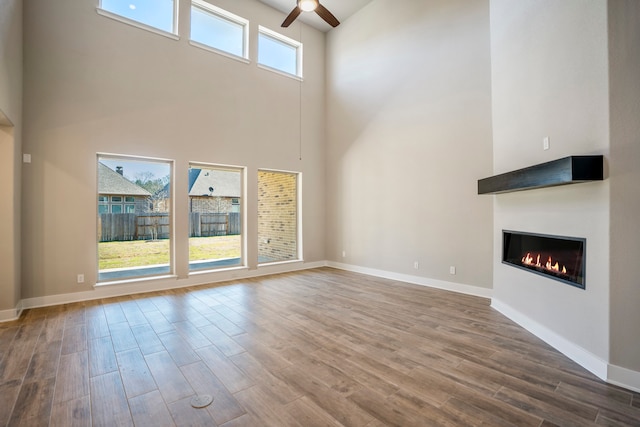 unfurnished living room with hardwood / wood-style flooring, ceiling fan, a high ceiling, and a wealth of natural light