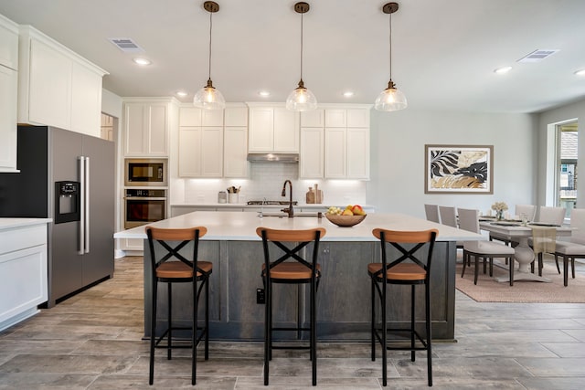 kitchen with a breakfast bar area, a center island with sink, stainless steel appliances, and decorative light fixtures