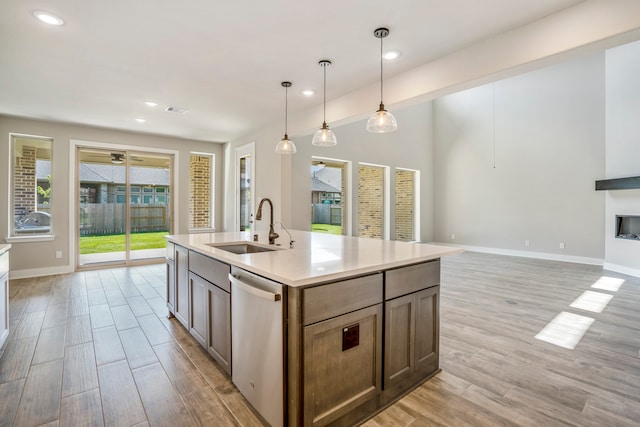 kitchen featuring sink, light hardwood / wood-style flooring, stainless steel dishwasher, an island with sink, and decorative light fixtures