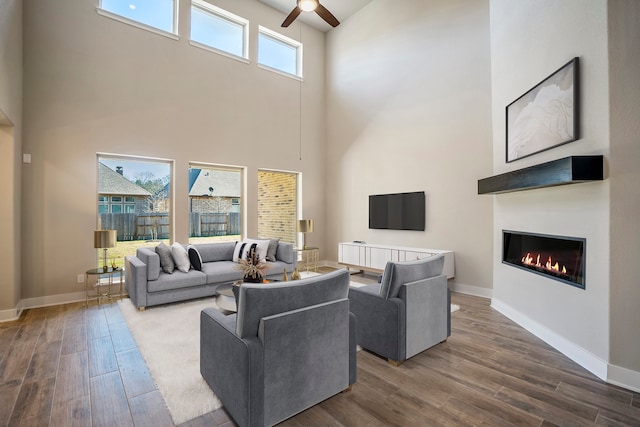 living room with a wealth of natural light, ceiling fan, wood-type flooring, and a high ceiling