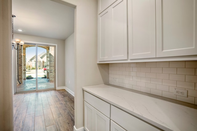 interior space featuring white cabinets, light wood-type flooring, tasteful backsplash, and light stone countertops