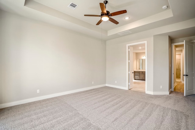 unfurnished bedroom featuring ceiling fan, light carpet, connected bathroom, and a tray ceiling