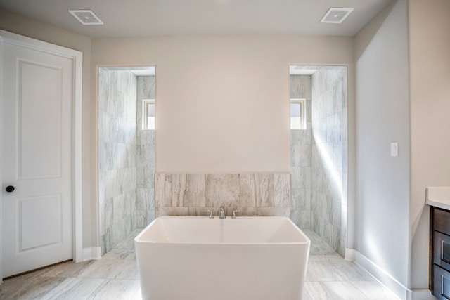 bathroom with a bathtub, vanity, and tile walls