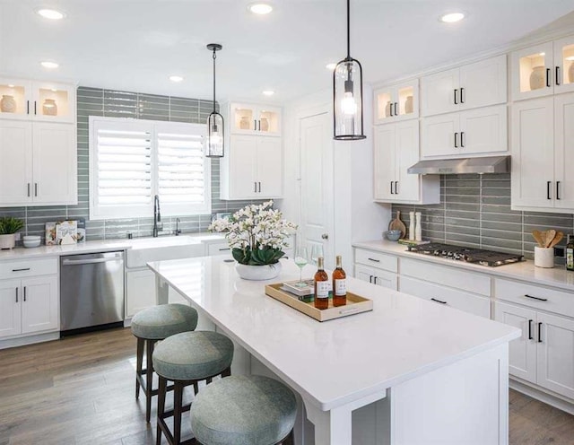 kitchen with white cabinetry, appliances with stainless steel finishes, extractor fan, a kitchen island, and hardwood / wood-style flooring