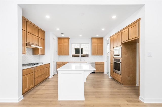 7427 Cattail Falls Ln, Porter, TX 77365 - kitchen with appliances with stainless steel finishes, a kitchen island, light wood-style floors, light countertops, and decorative backsplash