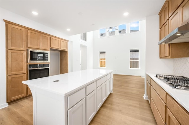 7427 Cattail Falls Ln, Porter, TX 77365 - kitchen with appliances with stainless steel finishes, light countertops, light wood finished floors, range hood, and a center island