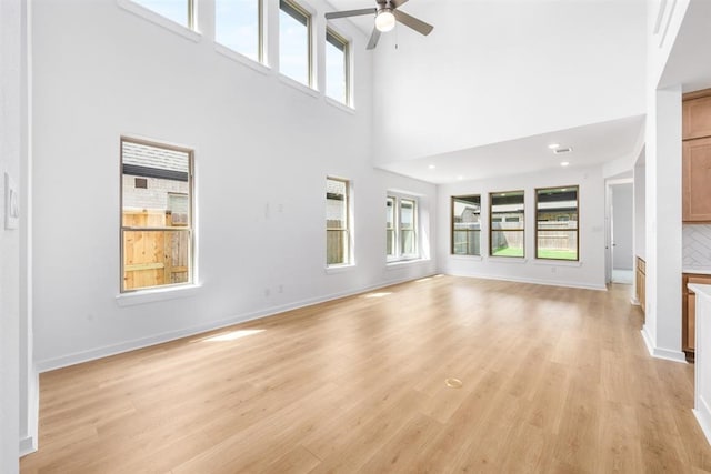 7427 Cattail Falls Ln, Porter, TX 77365 - unfurnished living room featuring a ceiling fan, plenty of natural light, light wood-type flooring, a towering ceiling, and baseboards