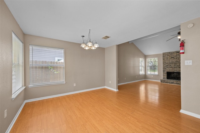 unfurnished living room with vaulted ceiling, a fireplace, light hardwood / wood-style flooring, and ceiling fan with notable chandelier