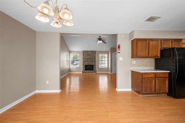 kitchen featuring light wood-type flooring, tasteful backsplash, black fridge, ceiling fan with notable chandelier, and a fireplace