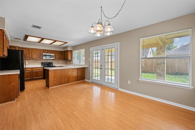 kitchen with french doors, black fridge, hanging light fixtures, kitchen peninsula, and a chandelier