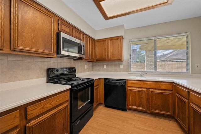 kitchen with black appliances, decorative backsplash, sink, and light hardwood / wood-style flooring